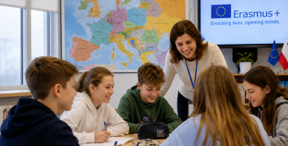 Na zdjęciu nauczycielka prowadzi zajęcia z grupą uczniów siedzących przy wspólnym stole. W tle widoczne są mapa Europy oraz ekran z logo programu Erasmus+, a także flagi Unii Europejskiej i Polski. Uczniowie wspólnie pracują nad zadaniem w przyjaznej atmosferze.