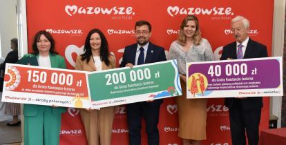 Cztery osoby trzymających w rękach symboliczne czeki z kwotami dofinansowania.