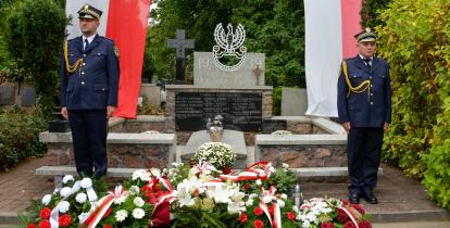 Dwóch strażników miejskich pełni wartę przy nagrobku na cmentarzu.