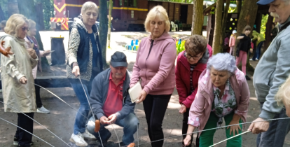 Grupa seniorów piecze kiełbaski nad ogniskiem