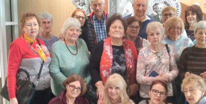 Grupa kilkunastu seniorek i kilku seniorów pozuje do wspólnego zdjęcia we wnętrzu budynku. Część osób stoi, a cztery kobiety siedzą lub klęczą z przodu.