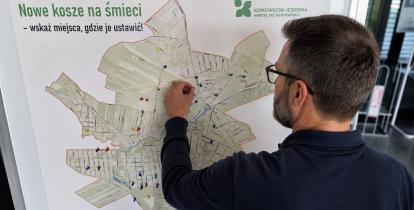 Mężczyzna przypina kolorową pinezkę do mapy gminy Konstancin-Jeziorna, wskazując proponowaną lokalizację nowego kosza na śmieci.