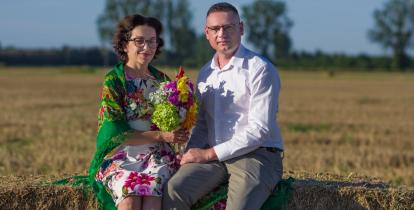 Kobieta i mężczyzna siedzą na beli skoszonego siana i wspólnie trzymają bukiet kwiatów. To starostowie dożynek 2026