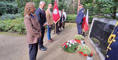 Władze gminy składają kwiaty przed pomnikiem katyńskim.