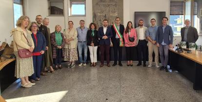 Grupowe zdjęcie delegacji Konstancina-Jeziorny i przedstawicieli Pisogne wykonane w sali posiedzeń włoskiego ratusza. W centrum stoi burmistrz Pisogne w szarfie w barwach włoskiej flagi, obok przedstawiciele obu miast.