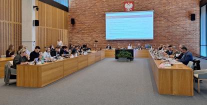 Sala obrad Rady Miejskiej Konstancin-Jeziorna podczas sesji. Radni siedzą przy stołach i uczestniczą w posiedzeniu.