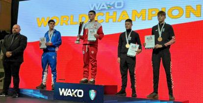 Kamil Kraczkowski , reprezentant Polski, odbiera złoty medal podczas ceremonii dekoracji na Mistrzostwach Świata WAKO. Zawodnicy stoją na podium na tle wielkiego ekranu z napisem "WAKO WORLD CHAMPION".