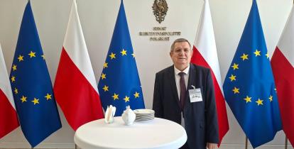 zdjęcie Wojciecha Guszkowskiego na tle flag Polski i UE