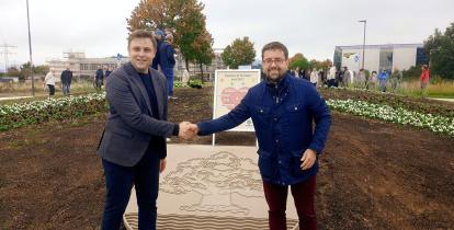 Burmistrzowie Michał Wiśniewski i Fabian Nitz ściskają dłonie na nowym rondzie w Denzlingen, przed kamiennym herbem Konstancina-Jeziorny. W tle tablica partnerska i uczestnicy uroczystości.