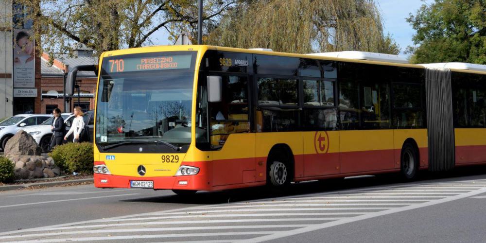 Ulica, po której jedzie czerwono-pomarańczowy autobus komunikacji miejskiej. Nad jego przednią szybą wyświetla się napis: 710.