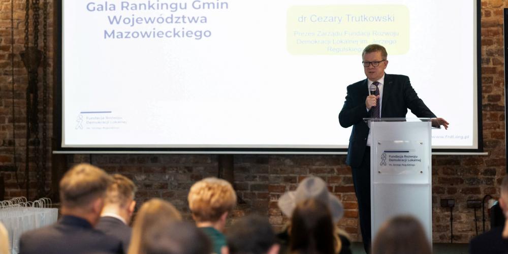 Mężczyzna stoi na scenie i trzyma w ręku mikrofon