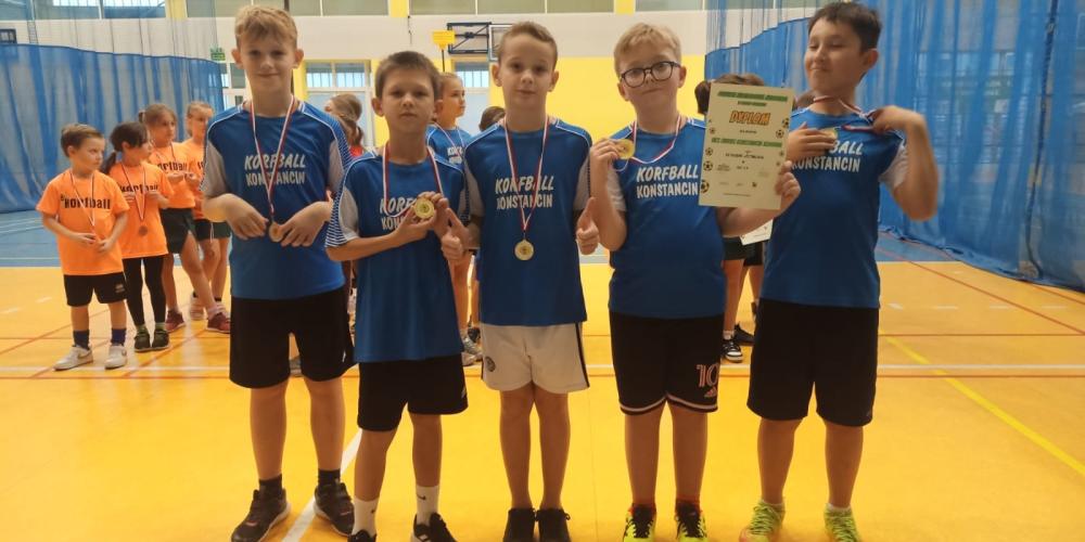 5 chłopców ubranych w niebieskie koszulki stoi obok siebie, na szyi mają medale. 