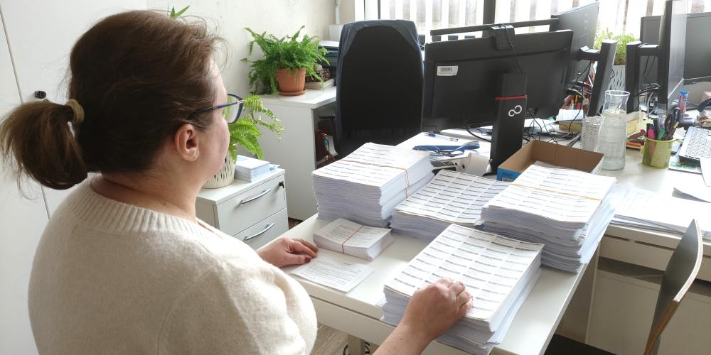 Kobieta siedzi przy biurku i pakuje listy do koperty. 