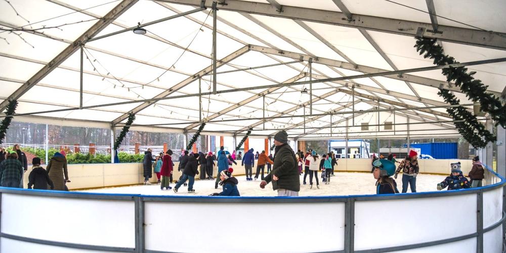 Kryte lodowisko, na którym dzieci i dorośli w zimowych ubraniach radośnie jeżdżą na łyżwach w otoczeniu świątecznych dekoracji.