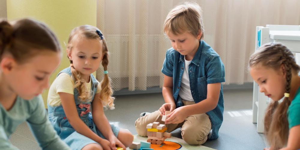 Dzieci bawiące się klockami, siedzą na podłodze w przedszkolu.