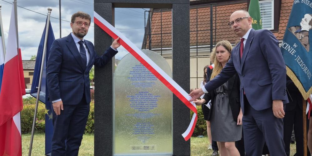 Uroczyste odsłonięcie pomnika upamiętniającego, z udziałem oficjeli i pocztów sztandarowych, odbywa się przy asyście flag narodowych i lokalnych.