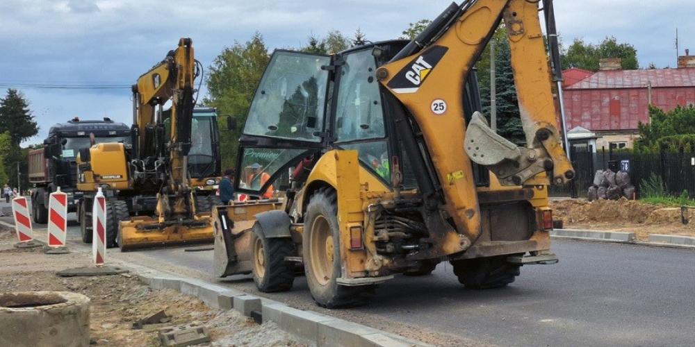 Maszyny budowlane prowadzące prace przy przebudowie drogi, z ułożonym już fragmentem nowego asfaltu i krawężnikami.