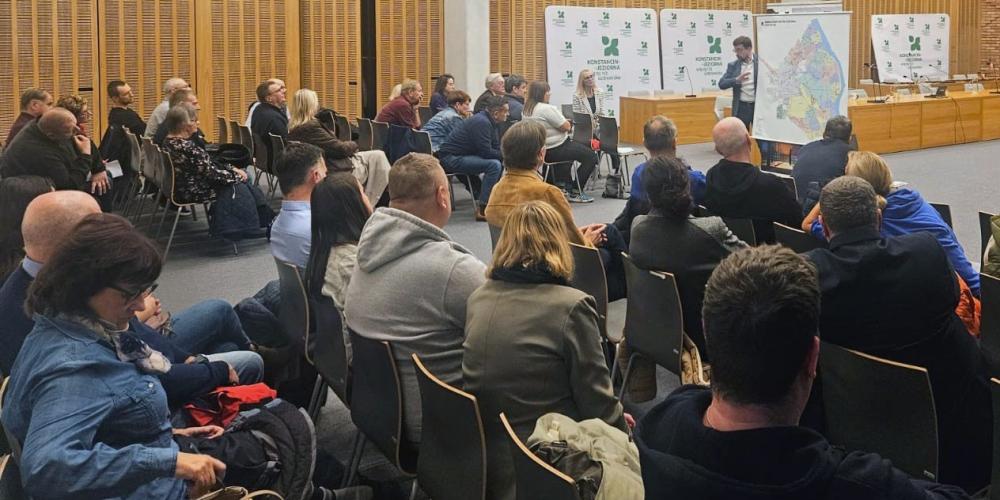 Grupa ludzi siedzi na krzesłach w sali konferencyjnej i słuch prezentacji.