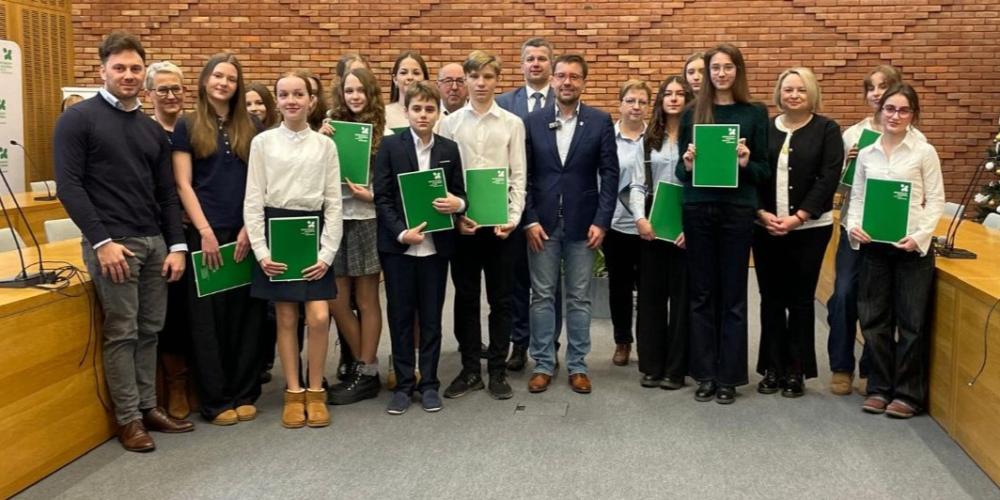 Grupa osób pozuje do zdjęcia na tle ściany z czerwonej cegły