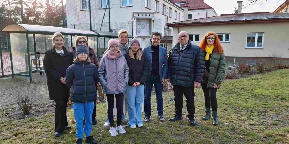 Grupa osób stoi przed stacją meterologiczną.