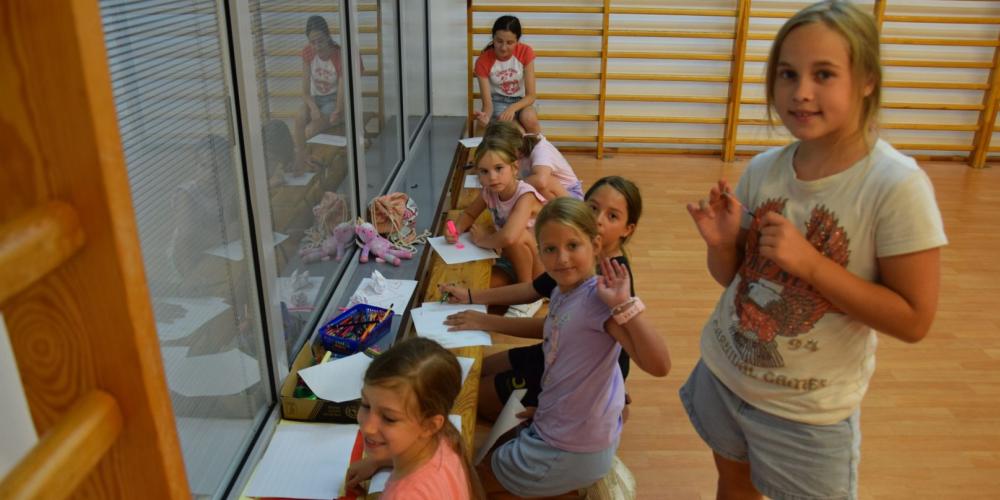 Zdjęcie grupy uśmiechniętych dzieci rysujących w sali gimnastycznej.