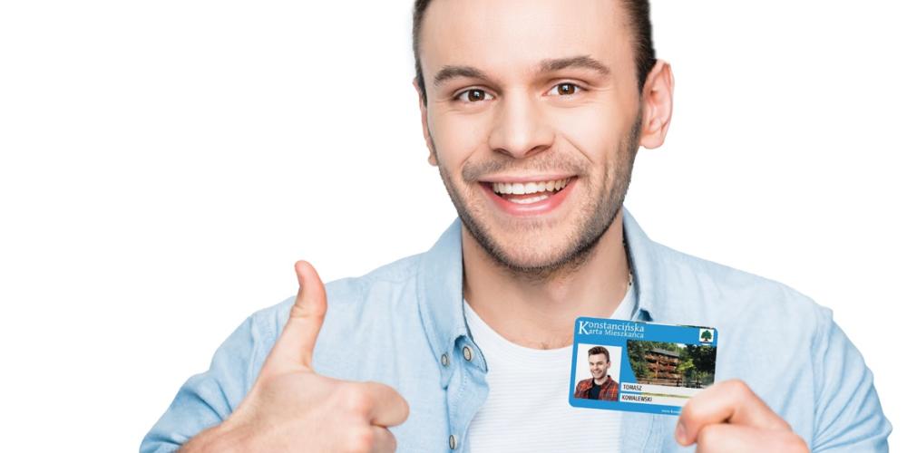 Uśmiechniety mężczyzna trzyma kartę mieszkańca i trzyma kciuk w górę.