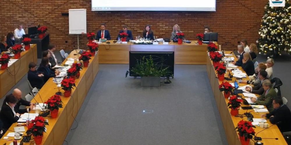 Sala obrad podczas sesji budżetowej – radni zasiadają przy długich stołach ustawionych w podkowę, a w tle widoczna jest świąteczna dekoracja z choinką i poinsecjami.
