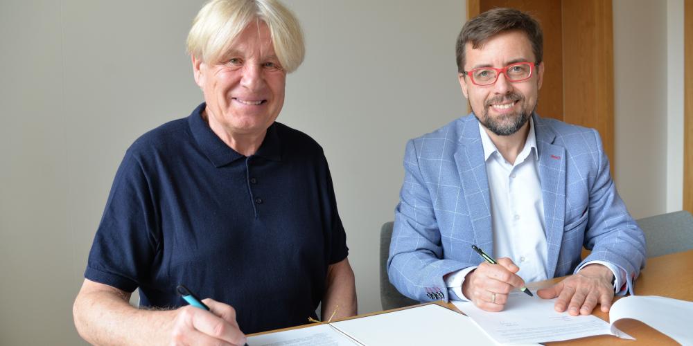 Dwóch mężczyzn siedzi przy stole i podpisuje dokumenty podczas zawarcia porozumienia dotyczącego współpracy Muzeum Villa la Fleur z Konstancińską Kartą Mieszkańca.