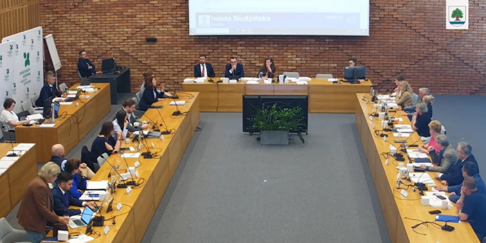Na zdjęciu sala obrad Rady Miejskiej Konstancin-Jeziorna podczas sesji – radni siedzą przy stołach ustawionych w kształcie podkowy, a obrady prowadzi prezydium zasiadające przy stole przewodniczącym.