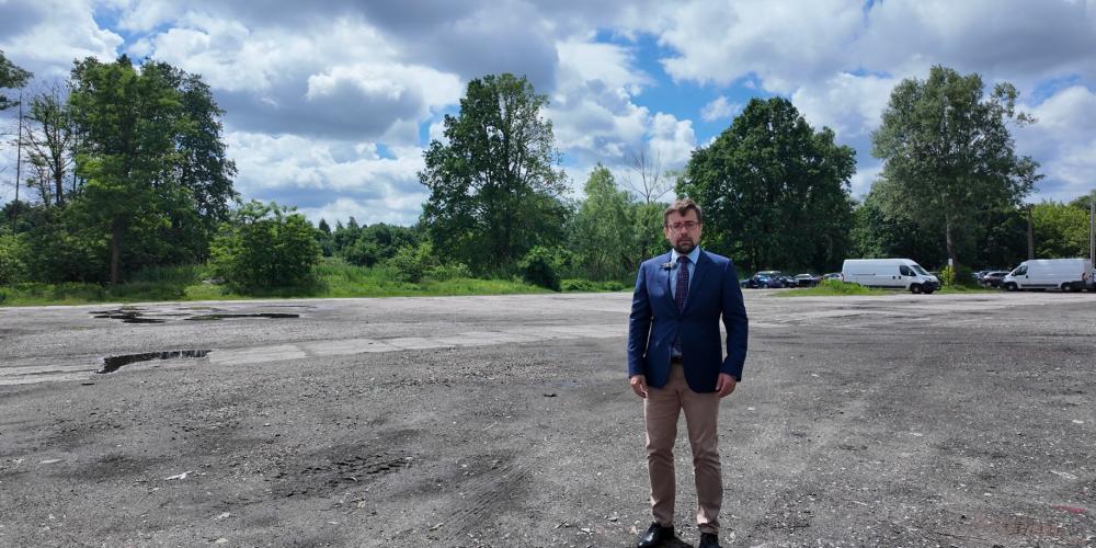 Mężczyzna stojący na rozległym terenie obecnego targowiska przy al. Wojska Polskiego, na tle zieleni i zachmurzonego nieba.