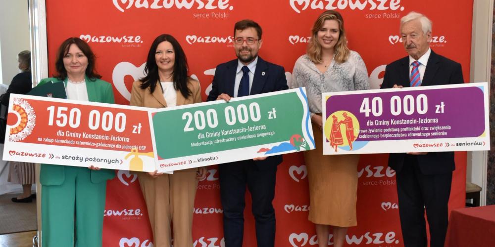 Cztery osoby trzymających w rękach symboliczne czeki z kwotami dofinansowania.