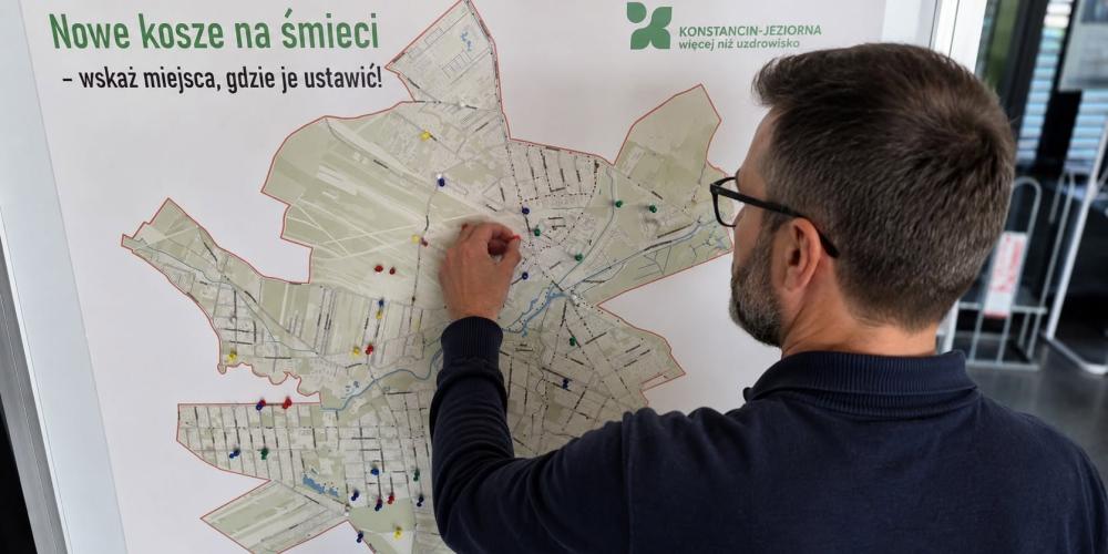Mężczyzna przypina kolorową pinezkę do mapy gminy Konstancin-Jeziorna, wskazując proponowaną lokalizację nowego kosza na śmieci.