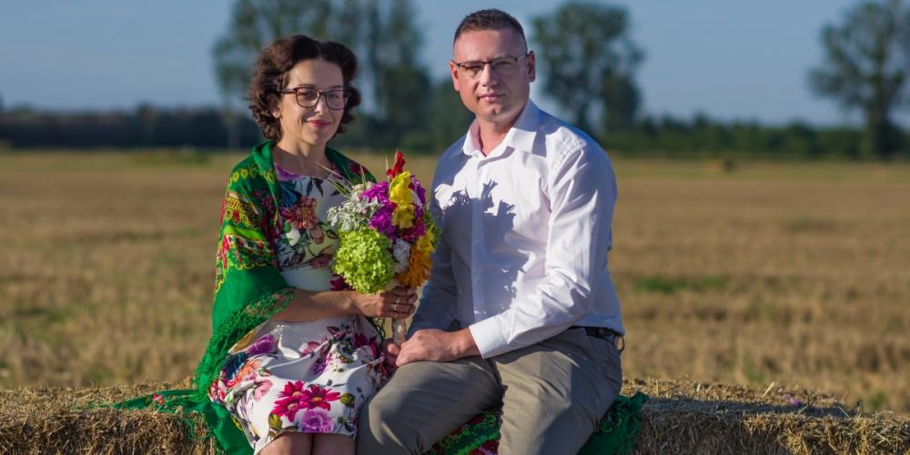 Kobieta i mężczyzna siedzą na beli skoszonego siana i wspólnie trzymają bukiet kwiatów. To starostowie dożynek 2026