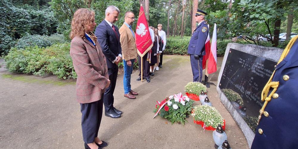 Władze gminy składają kwiaty przed pomnikiem katyńskim.