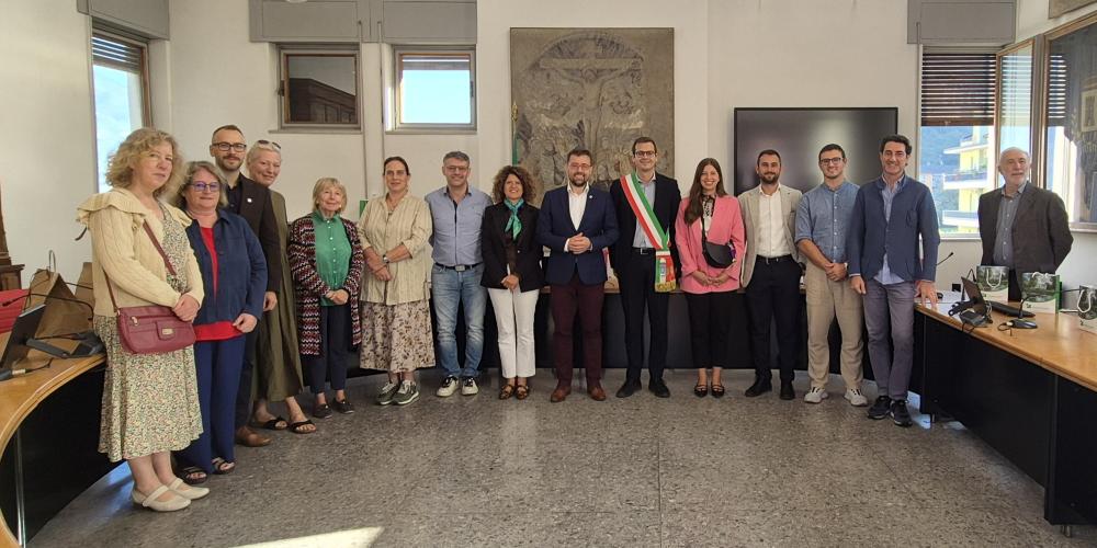 Grupowe zdjęcie delegacji Konstancina-Jeziorny i przedstawicieli Pisogne wykonane w sali posiedzeń włoskiego ratusza. W centrum stoi burmistrz Pisogne w szarfie w barwach włoskiej flagi, obok przedstawiciele obu miast.