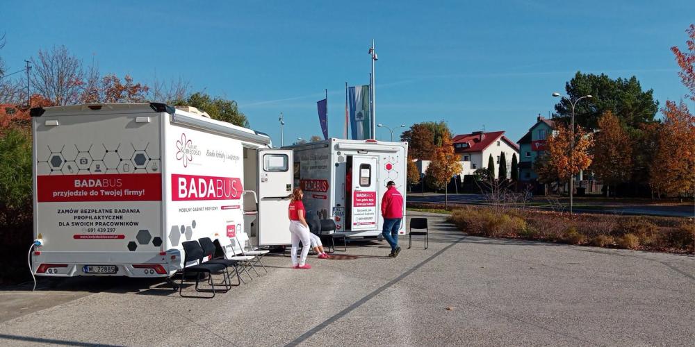 Przed urzędem stoją dwa mobilne gabinety medyczne oznaczone napisem „Badabus”, przy których znajdują się pracownicy oraz krzesła dla oczekujących pacjentów.