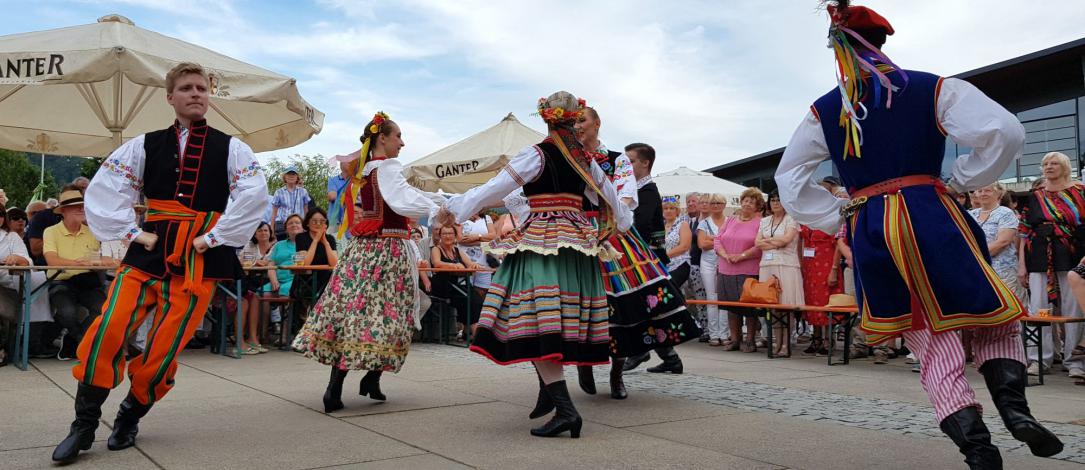 A group dancing in folk costumes in the middle of a large pacu surrounded by the audience