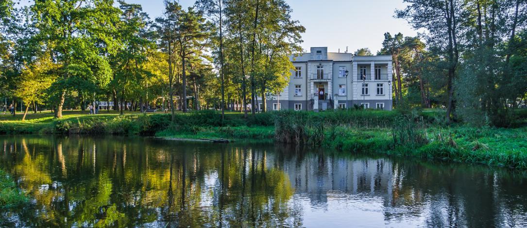 A magnificent villa standing on the river on which a canoe flows, a lot of trees and greenery around