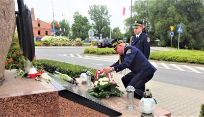 Dwóch mężczyzn, ubranych w stroje mundurowe Straży Miejskiej składają wieniec przed pomnikiem. 