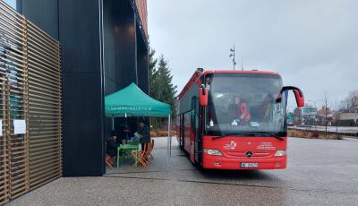 Na chodniku stoi duży czerwony autobus z białym napisem z boku Mobilny Punkt Poboru Krwi. Obok niego stoi zielony namiot. 