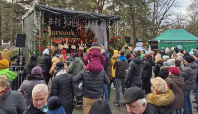 Występ lokalnych zespołów i chórów na scenie, z widocznymi świątecznymi dekoracjami i oświetleniem.