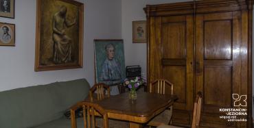 Wnętrze willi z dużą drewnianą szafą oraz meblami wypoczynkowymi (kanapą, stołem i krzesłami)/ 