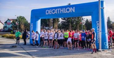 Kilkadziesiąt osób w strojach sportowych stoi za niebieską bramą startową z napisem Decathlon.