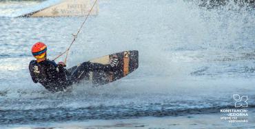 Mężczyzna na desce do wakeboardingu ciągnięty przez wyciąg, rozpryskująca się woda. 