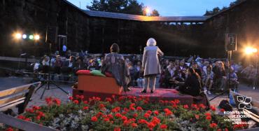Publiczność (głównie rodziny z dziećmi) siedzi na krzesłach i słucha występu trzech panów (opowiadaczy bajek). Występ odbywa się wieczorową porą na terenie tężni w Parku Zdrojowym