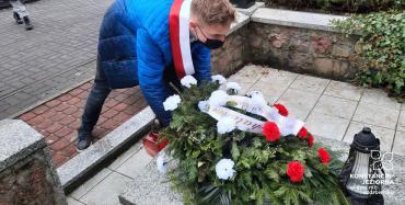 Uczeń w niebieskiej kurtce pochylony nad pominkiem, składa biało-czerwoną wiązankę z kwiatów. 