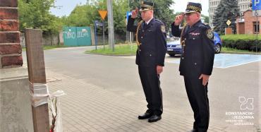   Dwóch mężczyzn, ubranych w stroje mundurowe Straży Miejskiej salutuje przed pomnikiem. 