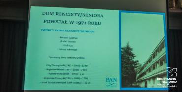 Sala. Na projektorze wyświetlany jest slajd, na którym jest napis Dom Rencisty/Seniora powstał w 1971 roku. Poniżej wymienieni są twórcy oraz dyrektorzy Domu Rencisty/Seniora.