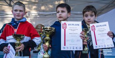 Trzech chłopców w wieku szkolnym stoi obok siebie w rzędzie. W rękach trzymają dyplomy i złote puchary.