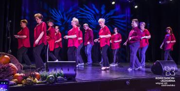 Na scenie występuje grupa dwunastu osób – dziesięć kobiet i dwóch mężczyzn. Każdy ubrany jest w czarne spodnie i czerwoną bluzkę. Wszyscy zwróceni są w lewą stronę. 